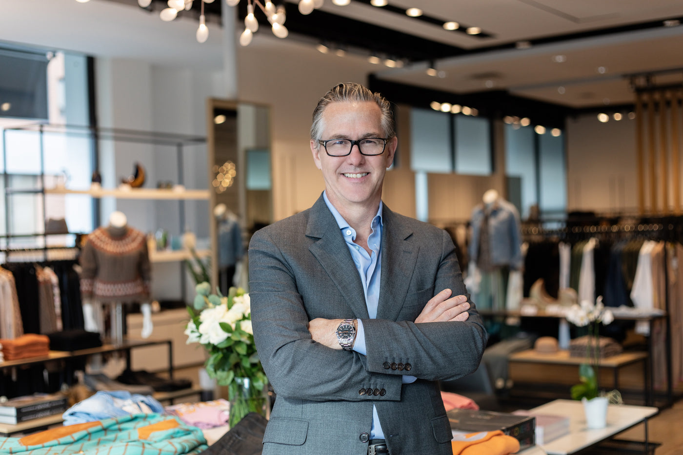 Portrait of Andrews President Darren Mason in a grey suit, standing in front of a retail store backdrop.  