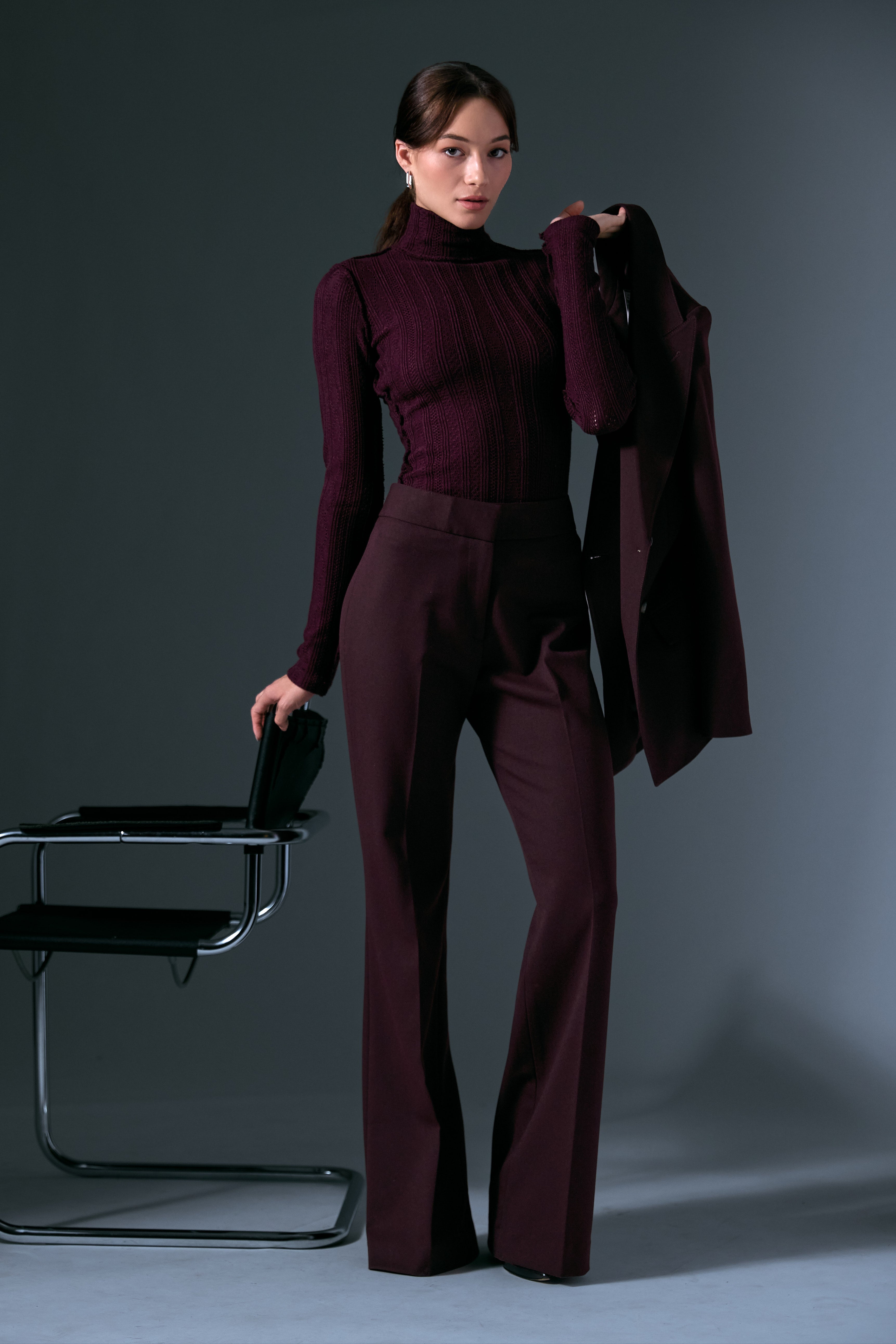 The Not A DB Blazer, Pointelle Knit Turtleneck, and Classic Pant by Smythe on a woman standing beside a Marcel Breuer Cantilever Chair.