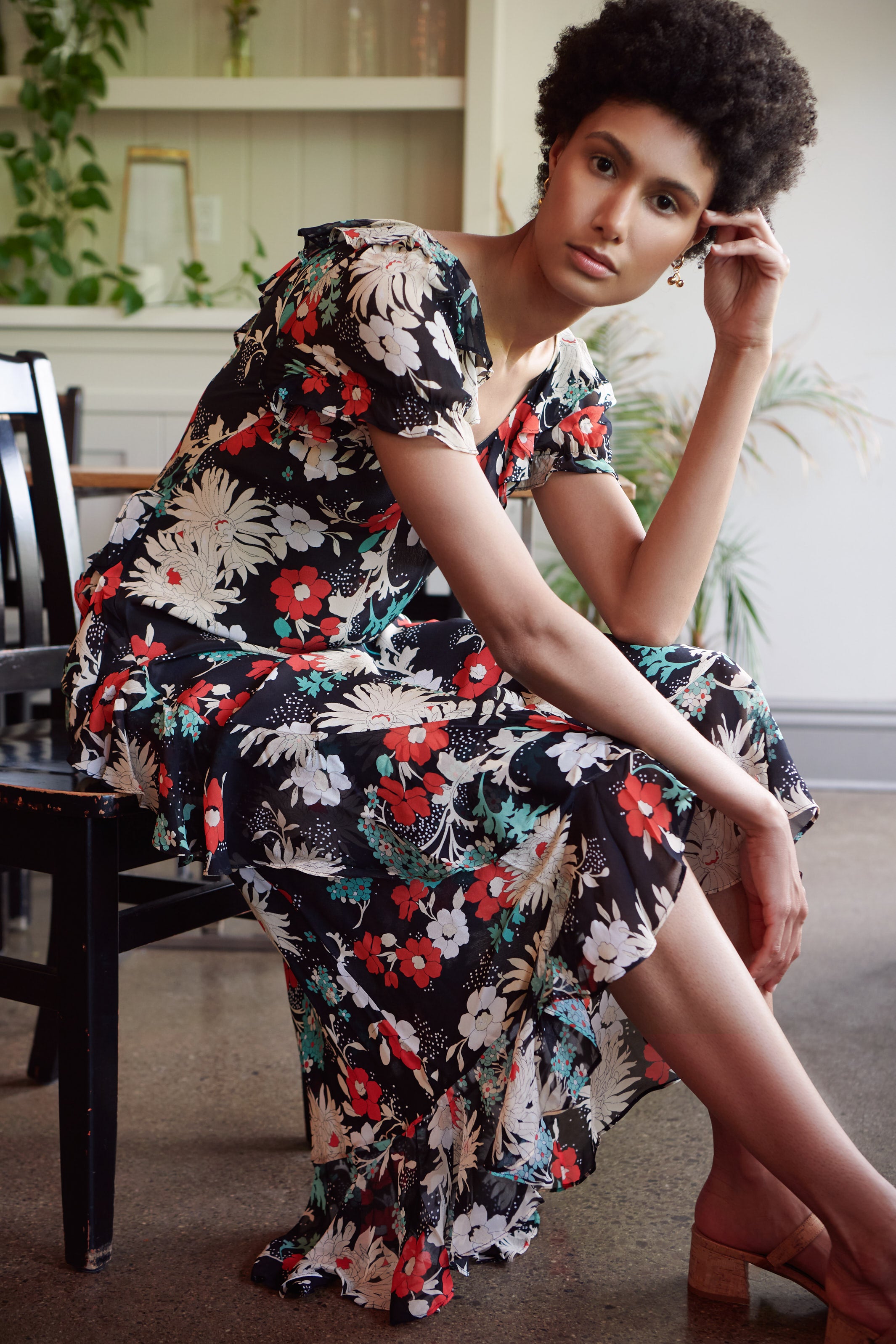 a woman wearing the Clementina Print Midi Dress by RIXO sits in a chair of a cafe