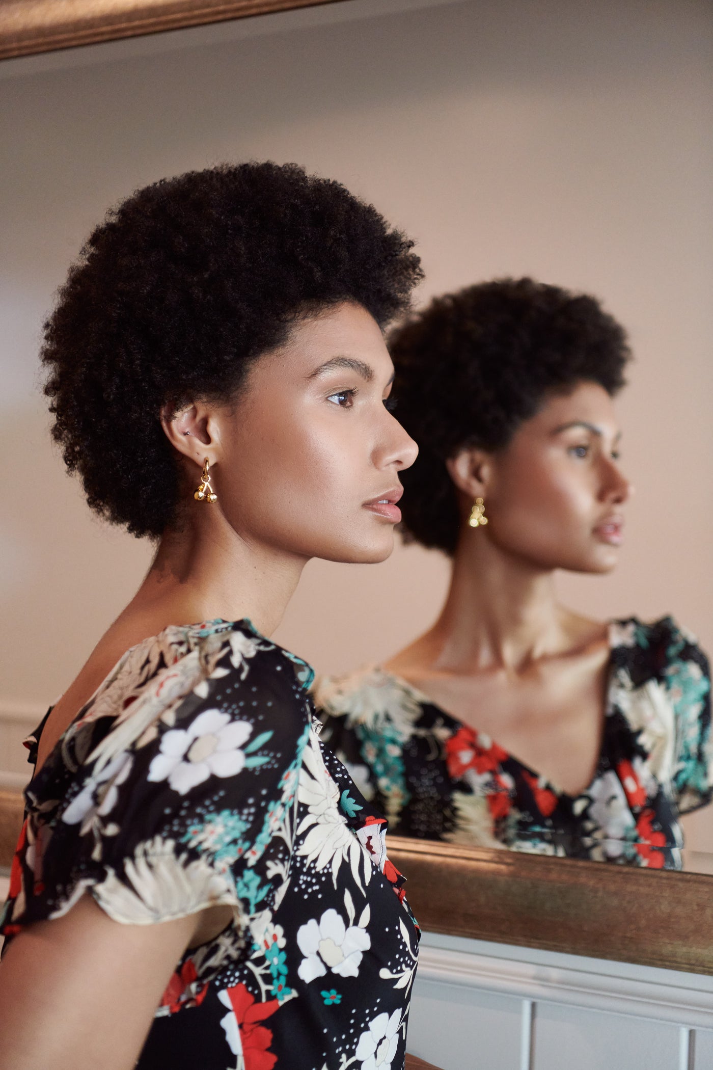 A woman wearing Clementina Print Midi Dress by RIXO accessorized with Jenny Bird earrings gazes past her reflection.